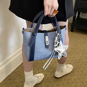 Side view of a large capacity blue denim bucket bag with a silver star pendant charm