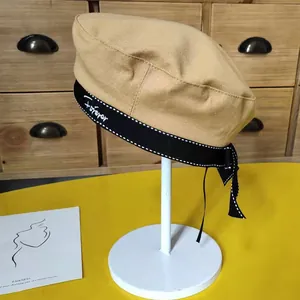 Detail of khaki beret hat with black bow ribbon and embroidered Forever letters.