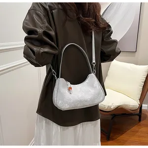 Side view of a white textured jacquard underarm bag on a model wearing a brown shirt