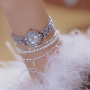 Close-up of elegant silver rhinestone watch paired with layered pearl bracelets on wrist
