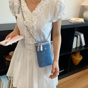 Detailed view of a denim crossbody phone bag with camellia charm and silver chain.