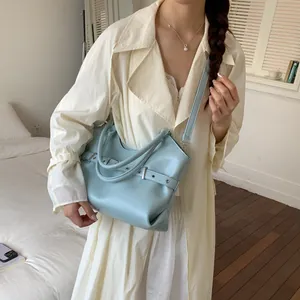 Fashionable light blue leather tote bag with belt detail shown on model in a cozy room