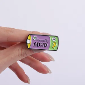 Close-up of "Powered by ADHD" battery enamel pin held in hand for backpack decor