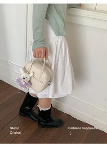 Detailansicht einer cremeweißen kleinen quadratischen Handtasche mit Bärenanhänger