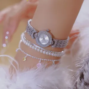 Close-up of elegant silver crystal watch and pearl bracelets with feather background