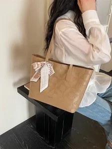 Stylish large tan tote bag with geometric embossed pattern and decorative scarf accessory