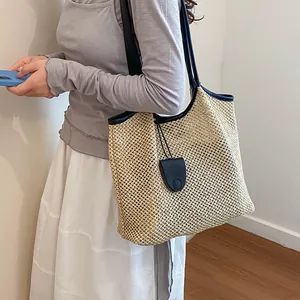 Dettaglio di una grande borsa tote in paglia intrecciata con manici neri indossata
