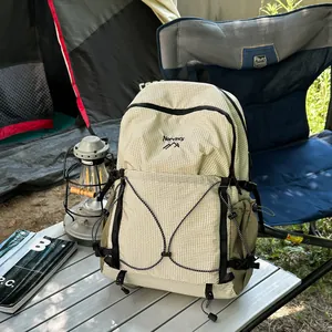 Sac à dos de randonnée léger à carreaux beige dans une scène de camping extérieur.