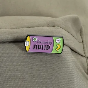 Close-up of a Powered by ADHD battery-shaped enamel pin on a green fabric backpack.