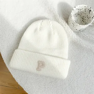 Close-up of white knitted beanie with embroidered P letter and textured pattern