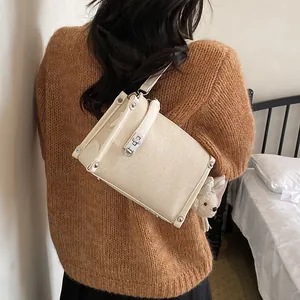 Back view of a stylish beige straw crossbody bag with white trim worn over a brown knit sweater