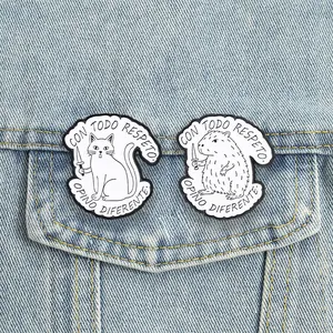 Funny cat and capybara enamel pins shown pinned on a denim jacket pocket detail