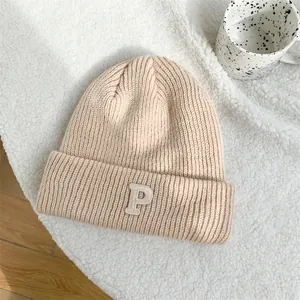 Detail showing the thick knit texture and embroidered P letter on the beige beanie