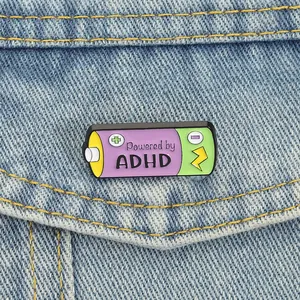 Close-up detail of Powered by ADHD battery enamel pin pinned on a denim jacket pocket