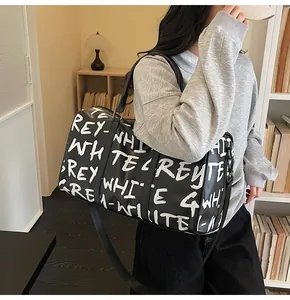 Large capacity black graffiti travel duffel bag held by a model in a cozy interior
