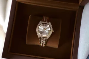 Primer plano detallado de un reloj de lujo para mujer en tono dorado con cristales brillantes en caja.