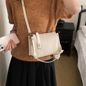 Model wearing a stylish beige canvas crossbody pillow bag with silver lock detail