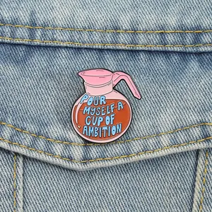 Enamel pin brooch shaped like a coffee pot with motivational quote on a denim jacket