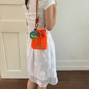 Detailed view of a bright orange bucket bag featuring a banana charm worn by a model