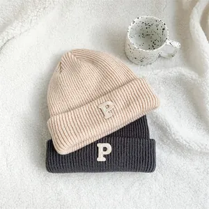 Detailed view of two stylish knit beanies with embroidered P letter on white sherpa