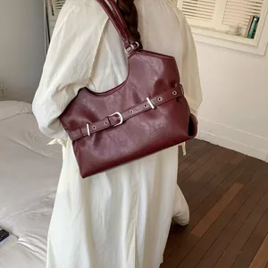 Detail view of a burgundy leather underarm tote bag with decorative buckle strap