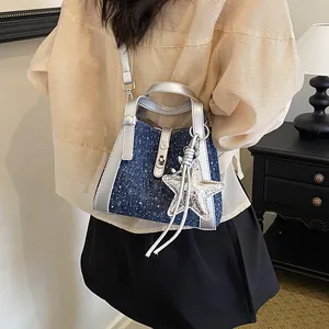 Detail of a chic denim bucket bag with silver trim and star charm worn by a model