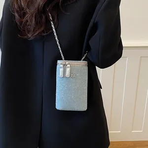 Close-up view of light blue denim crossbody phone bag with chain strap and flower charm.