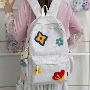Close-up of grey fabric backpack with colorful flower embroidery and plush bunny charm.