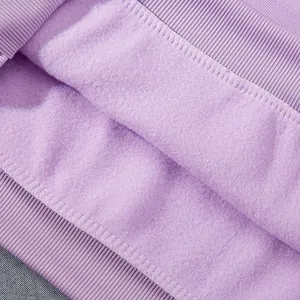 Détail macro montrant la doublure polaire violette douce et les coutures du sweat à capuche.