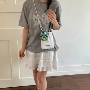 Minimalist white bucket crossbody bag with decorative rope strap and banana charm