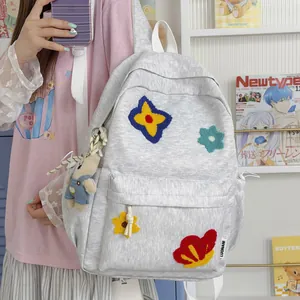Cute grey student backpack with colorful flower patches and bear charm shown being worn