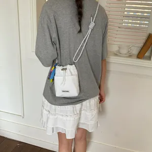White mesh bucket bag with grey rope strap worn by a woman in a casual setting
