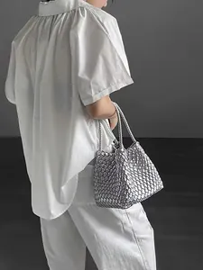 A detailed view of a silver woven basket handbag carried by a model in white clothes