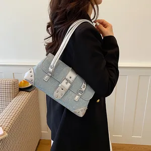 Side view of blue denim baguette bag with silver trim worn by a model in office setting.