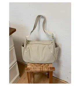Large beige nylon travel tote bag displayed on a rustic woven stool in a bright room