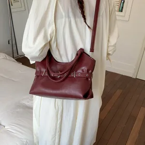 Close-up of a stylish burgundy leather tote bag with buckle detail worn by a model