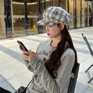 Stylish black and white plaid baker boy hat worn by a model in an outdoor setting