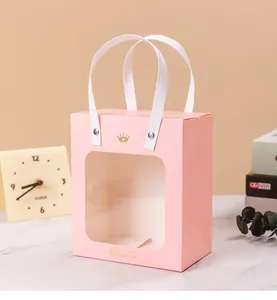 Close-up view of pink paper gift bag featuring gold crown logo and a clear window