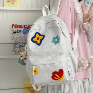 Detailed view of light gray school backpack with colorful embroidered flower patches and bear charm