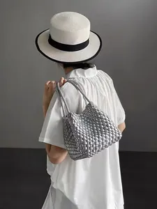 Close-up of a stylish silver woven bucket bag carried by a woman in a white dress and hat