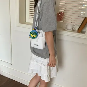 Detail view of a white canvas bucket bag with a thick rope strap and banana charm