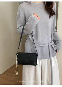 Borsa sottobraccio minimalista in pelle nera mostrata su una modella chic.