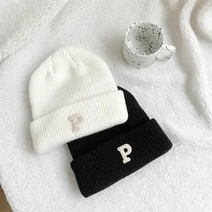 Detailed close-up of white and black knitted beanies featuring 'P' letter embroidery design