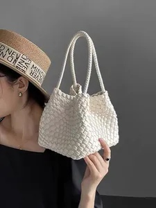 Close-up of minimalist white woven bucket bag held by an elegant woman wearing a straw hat