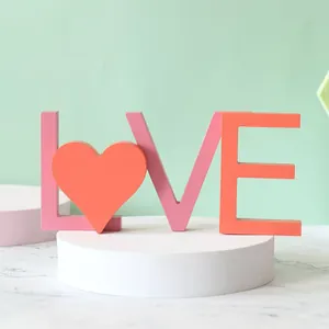 Gros plan d'un signe LOVE en bois rose et orange avec cœur sur un piédestal blanc.