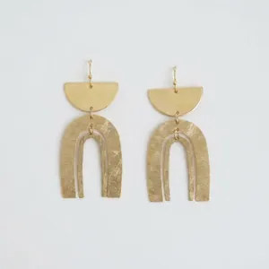 Détail montrant la finition dorée mate et le design en arche des boucles d'oreilles