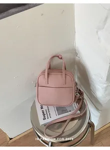 Detailansicht einer rosa Mini-Quadrat-Handtasche aus Kunstleder auf einem silbernen Hocker.
