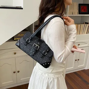 Detail view of black denim baguette bag with silver studs and buckle strap on model