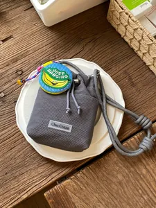 Stylish grey mesh drawstring bucket bag with banana charm on a rustic wooden table.