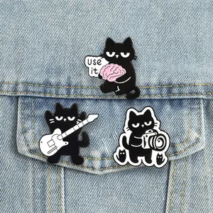 Detailed view of three cartoon black cat enamel pins pinned on denim jacket pockets